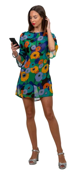 Yarı şeffaf mini elbiseli bir kadın ayakta duruyor ve beyaz arka planda izole edilmiş telefonuna bakıyor.