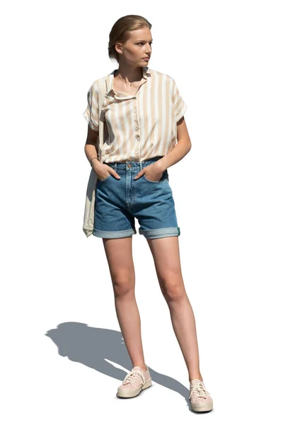 Güneşin altında elini cebine sokup beyaz arka planda öylesine dikilen güzel, genç bir kadın.