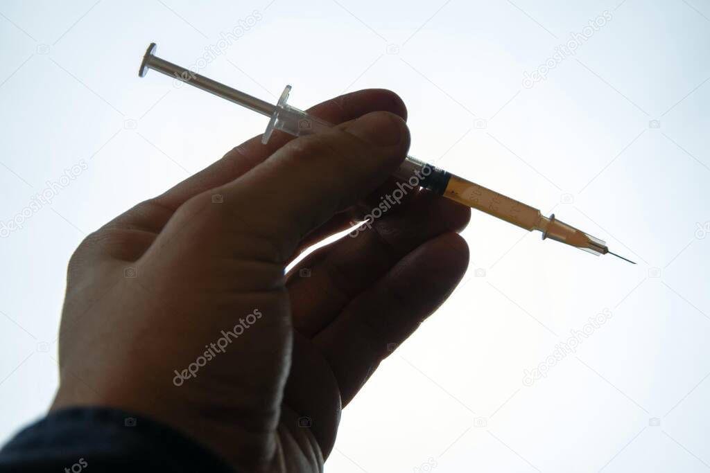 the darkened hand of the addict keeps a syringe with a narcotic solution inside against a background of bright light