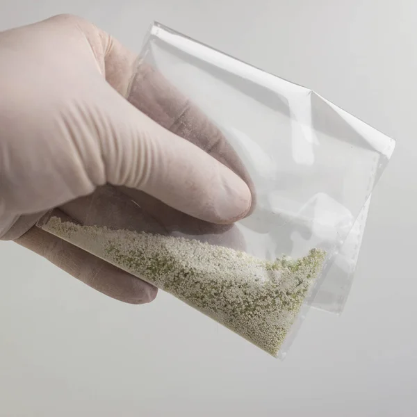 new drugs synthetic production: transparent bag with a narcotic crystalline substance, short focus, white background, changed contrast