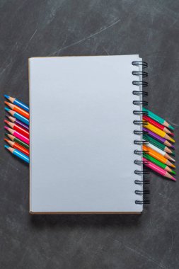 Beyaz defter, arka planda çok renkli kalemler üzerine kuruludur.