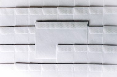 Ofisteki masanın üstünde duran boş beyaz zarflar dizisi. Bir zarf sıradan çıkarılmış, kısa odaklanma, tonlama.