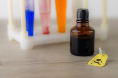 Test tüplerinin arka planında kafatası ve kemikleri olan sarı uyarı etiketi ve kimyasal hazırlıkları olan laboratuvar kapları, kısa odaklı