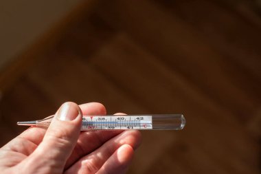 Koronavirüsün belirtileri: kişinin elinde bir cıva termometresi vardır, bu da sıcaklığın arttığını gösterir. koyu arkaplan