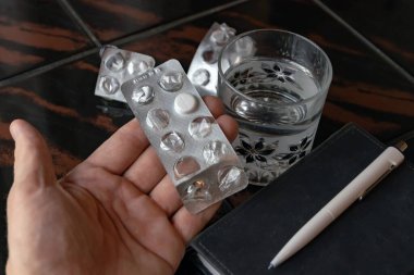 Adam elinde son hapla su topladı, su toplayan bir arka plan, bir bardak ve bir defter.