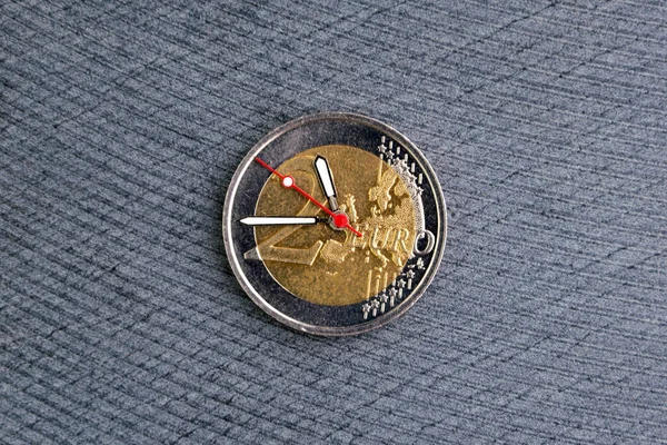 time to benefit: 2 euro coin with hour hands on a dark background, short focus, close