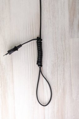 Enerji bağımlılığı kavramı: fişi olan bir elektrik kablosundan yapılmış menteşe döngüsü, tahta arka planda, seçici odak