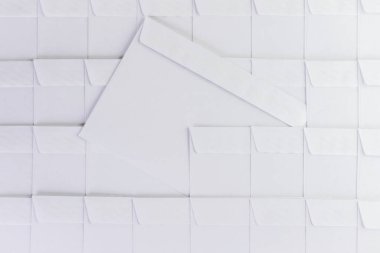 Ofisteki masanın üstünde duran boş beyaz zarflar dizisi. Bir zarf sıradan çıkarılmış, kısa odaklanma, tonlama.