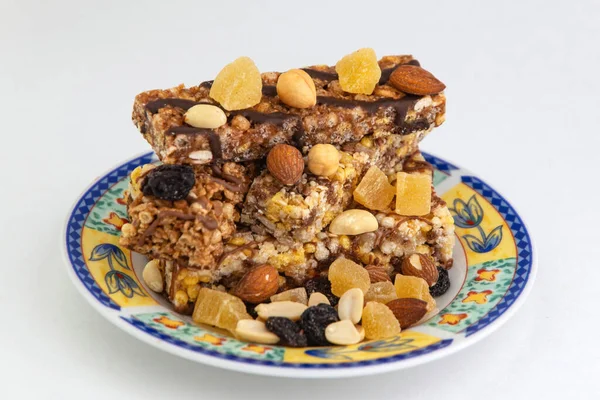 vegan dessert: several cereal bars with nuts, raisins and honey, in a colorful plate on white, short focus