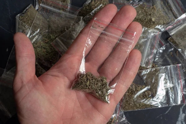 Suç delili bir paket içinde bir kişinin elinde bir sürü paketlenmiş esrar arka planında koyu bir surfac üzerinde yatıyor
