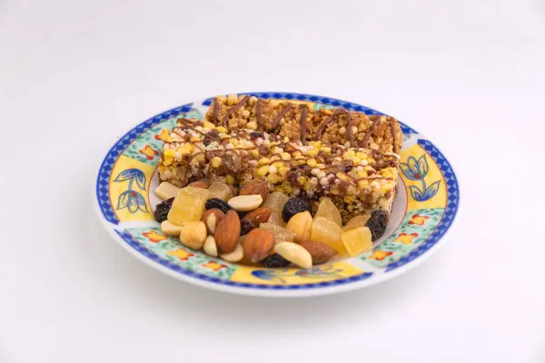 vegan dessert: several cereal bars with raisins and honey are on a bright plate, a lot of nuts and candied fruits are lying around, short focus