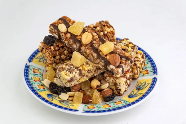 vegan dessert: several cereal bars with nuts, raisins and honey, in a colorful plate on white, short focus