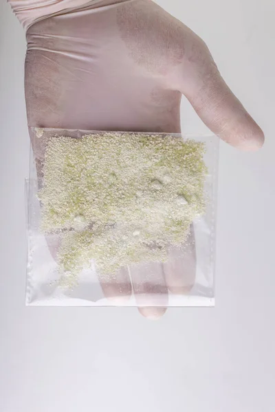 new drugs synthetic production: transparent bag with a narcotic crystalline substance, short focus, white background, changed contrast