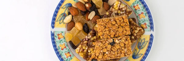 vegan dessert: several cereal bars with raisins and honey are on a bright plate, a lot of nuts and candied fruits are lying around, short focus
