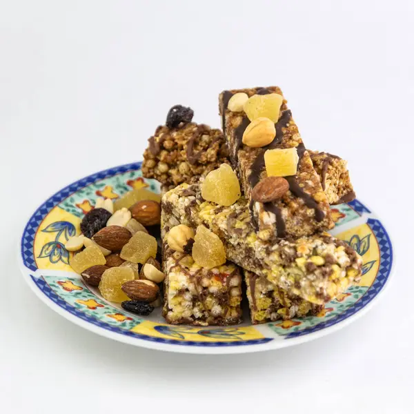 vegan dessert: several cereal bars with nuts, raisins and honey, in a colorful plate on white, short focus