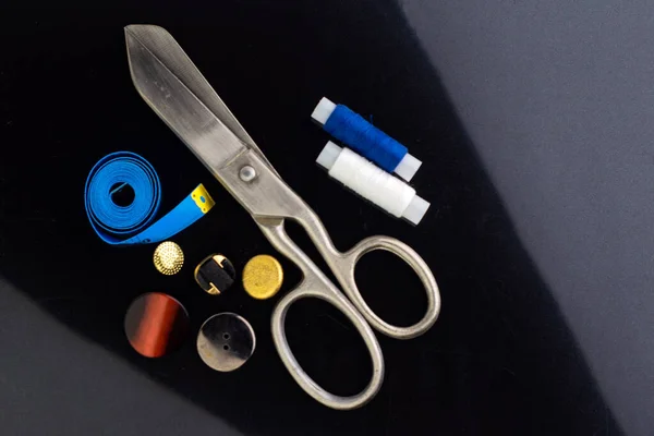 vintage big seamstress scissors, measuring blue tape and buttons on black background. short focus