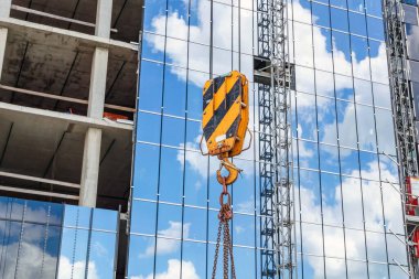 Binaların yapımı: bir vinç kancası, arka plandaki zincirler ve kablolar cama yansıyor.