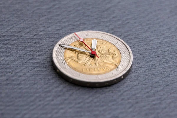 time to benefit: 2 euro coin with hour hands on a dark background, short focus, close