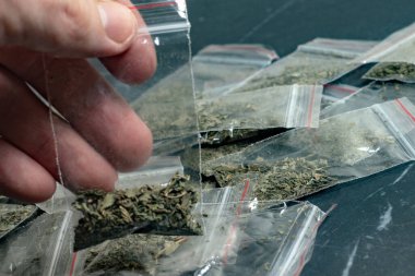 Suç delili bir paket içinde bir kişinin elinde bir sürü paketlenmiş esrar arka planında koyu bir surfac üzerinde yatıyor
