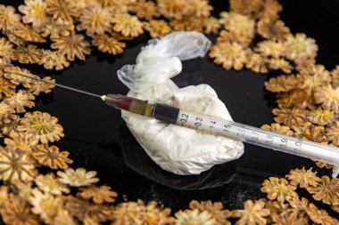 Uyuşturucu: bir şırınga ve bir torba eroin siyah bir tabakta kurumuş haşhaş bitkisinin parçaları arasında, yakın. kısa odak