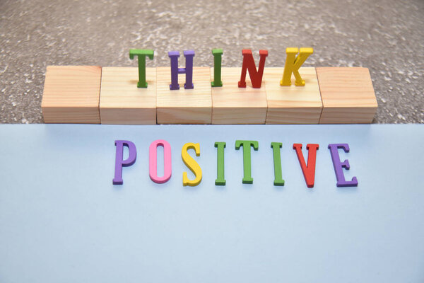 THINK wording stand on the wooden blocks with POSITIVE text lie down in the baby blue paper. Lifestyle concept.