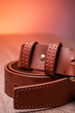 Deri kahverengi kemer, turuncu arka plandaki ahşap bir tahtanın üzerinde duruyor.