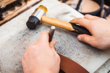 Ustanın ellerinde deride delikler açmak için bir araç. Elde çekiç.