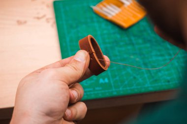 Eller kahverengi bir kemeri iplik ve iğneyle diker.