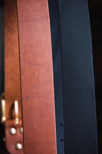 Siyah arka planda altın tokalı mavi ve kahverengi deri kemer büyük bir plan.