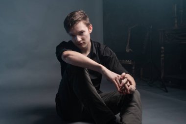 Ciddi bir genç adam gri bir arka planda oturuyor.