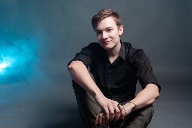 Adam gri arka planda oturuyor ve gülümsüyor.