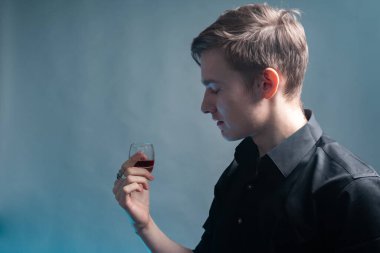 Genç bir adam gri arka planda bir bardak rom tutuyor.