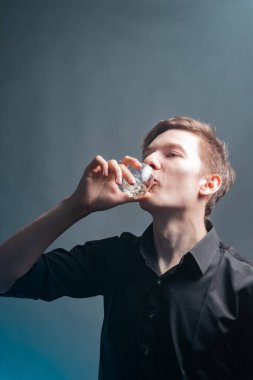 Adam gri arka planda bir bardaktan viski içiyor.