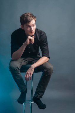 Siyah gömlekli adam gri arka planda bar taburesinde oturuyor.