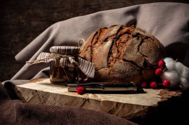 Bıçak ekmeğin yanında ve kahverengi arka planda bir kavanoz bisküvi var.