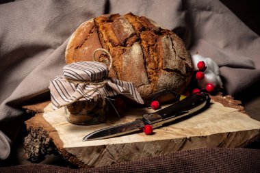 Bıçak ekmeğin yanında ve kahverengi arka planda bir kavanoz bisküvi var.