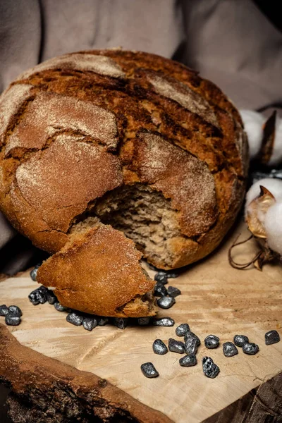 A piece of bitten bread next to a whole loaf on a wooden background