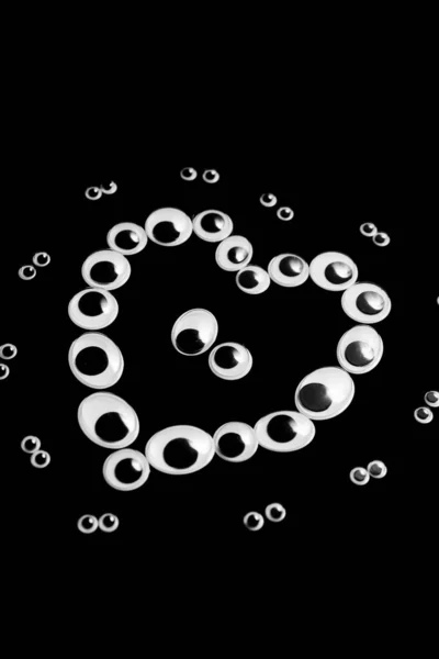 Puppet eyes of different sizes, laid out in the shape of a heart on a black background — Stock Photo, Image