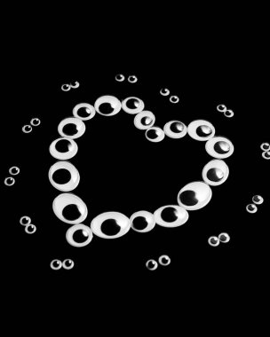 Farklı boyutlarda kukla gözler, siyah bir arka planda kalp şeklinde serilmiş.