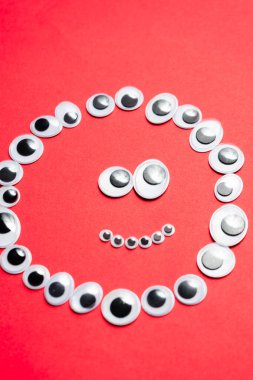 Tek renkli kırmızı bir arka planda oyuncak gözlerle gülümsemek.