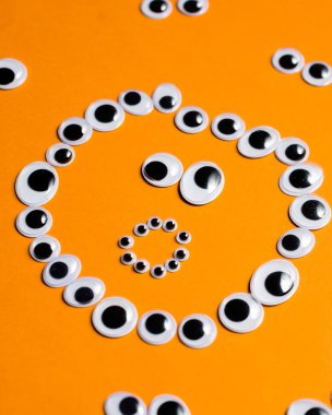 Turuncu bir arka plandaki diğer gözlerin etrafındaki oyuncak gözlerden gelen şaşkın gülen yüz.