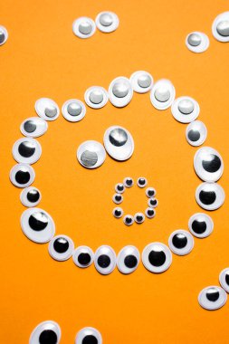 Turuncu bir arka plandaki diğer gözlerin etrafındaki oyuncak gözlerden gelen şaşkın gülen yüz.