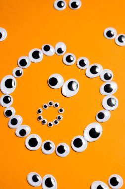 Turuncu bir arka plandaki diğer gözlerin etrafındaki oyuncak gözlerden gelen şaşkın gülen yüz.