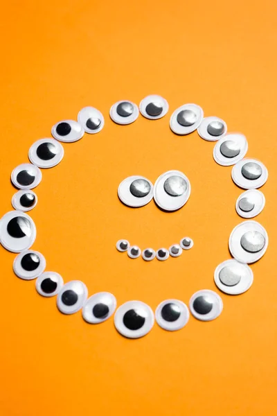 Emotionales Smiley-Gesicht aus Spielzeugaugen auf orangefarbenem Hintergrund lizenzfreie Stockbilder