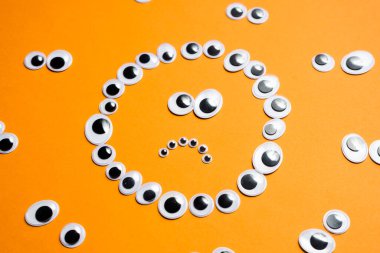 Turuncu bir arka plandaki diğer gözlerin etrafındaki oyuncak gözlerden hüzünlü gülen yüz.