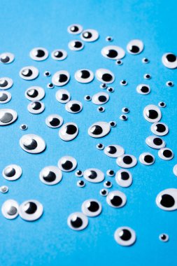 Farklı boyutlarda oyuncak gözler mavi arka plana saçılmış.