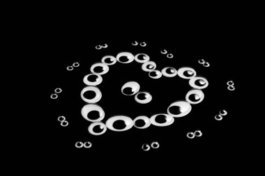 Farklı boyutlarda kukla gözler, siyah bir arka planda kalp şeklinde serilmiş.