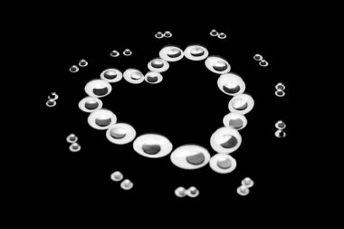 Farklı boyutlarda kukla gözler, siyah bir arka planda kalp şeklinde serilmiş.