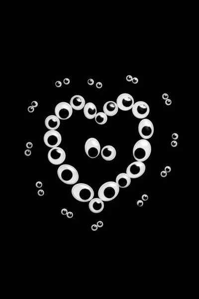 Olhos de marionete de tamanhos diferentes, dispostos na forma de um coração em um fundo preto — Fotografia de Stock