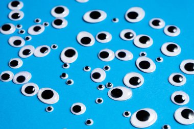 Farklı boyutlarda oyuncak gözler mavi arka plana saçılmış.